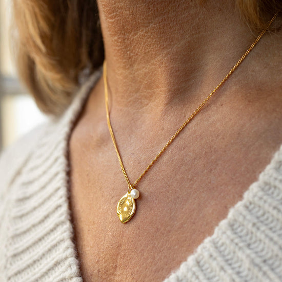 Gold necklace with a leaf-shaped pendant worn by a person