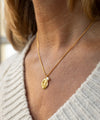 Gold necklace with a leaf-shaped pendant worn by a person