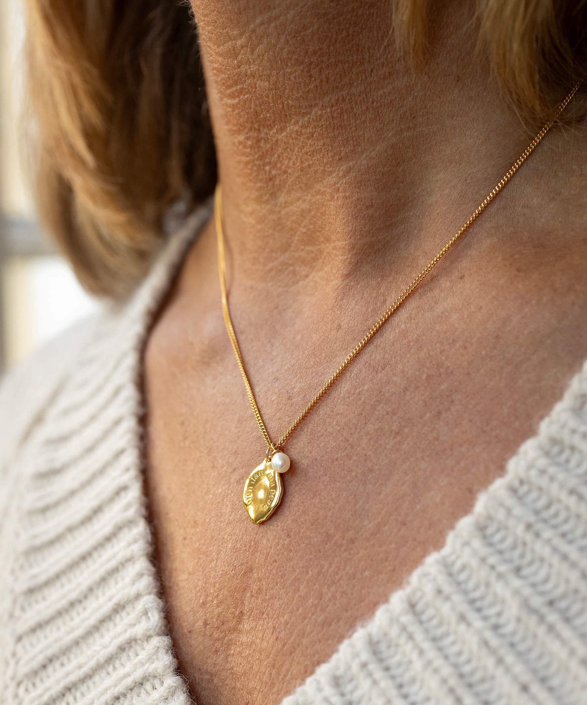 Gold necklace with a leaf-shaped pendant worn by a person