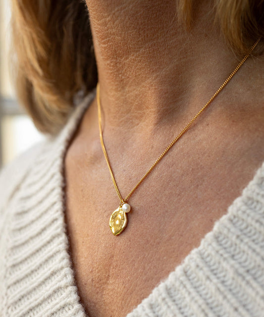 Gold necklace with a leaf-shaped pendant worn by a person