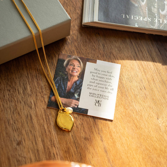Gold necklace with a heart-shaped pendant on a wooden surface next to a card and book.