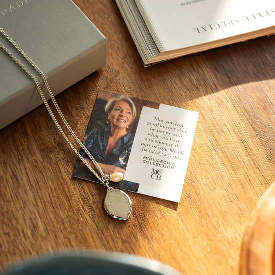 Necklace with pendant on a card featuring a photo and text, placed on a wooden surface next to an open book.
