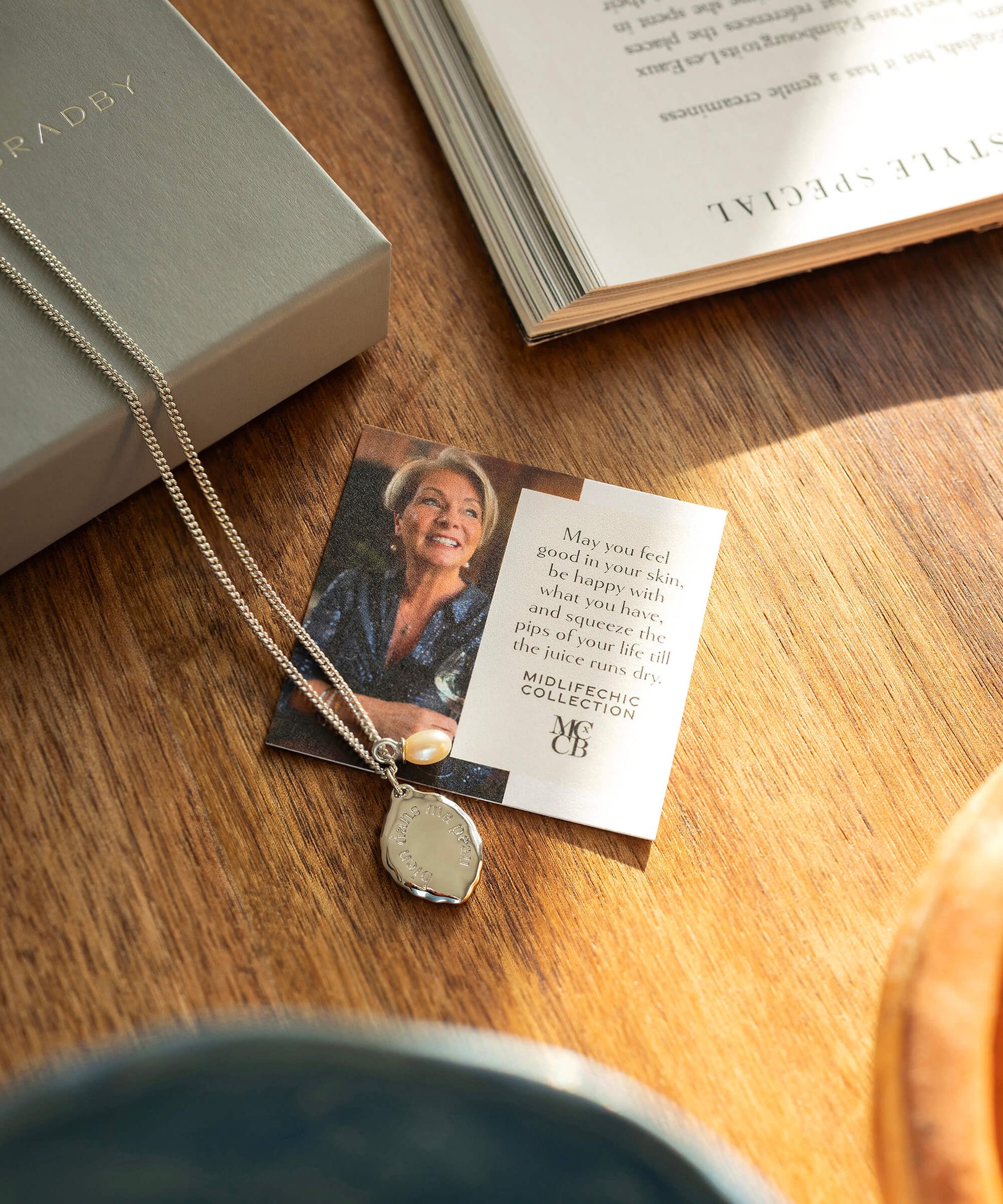 Necklace with pendant on a card featuring a photo and text, placed on a wooden surface next to an open book.