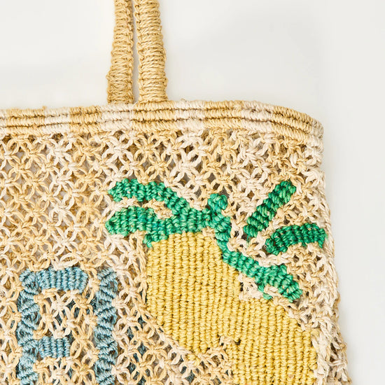 yellow and beige string bag with slogan on white background zoomed in 
