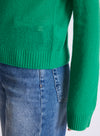 Close-up of a bright green knit sweater worn with blue jeans, showing the ribbed hem and sleeve cuff against a plain light background.