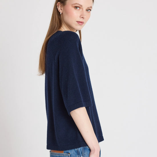 Woman wearing a navy blue sweater and jeans on a light gray background