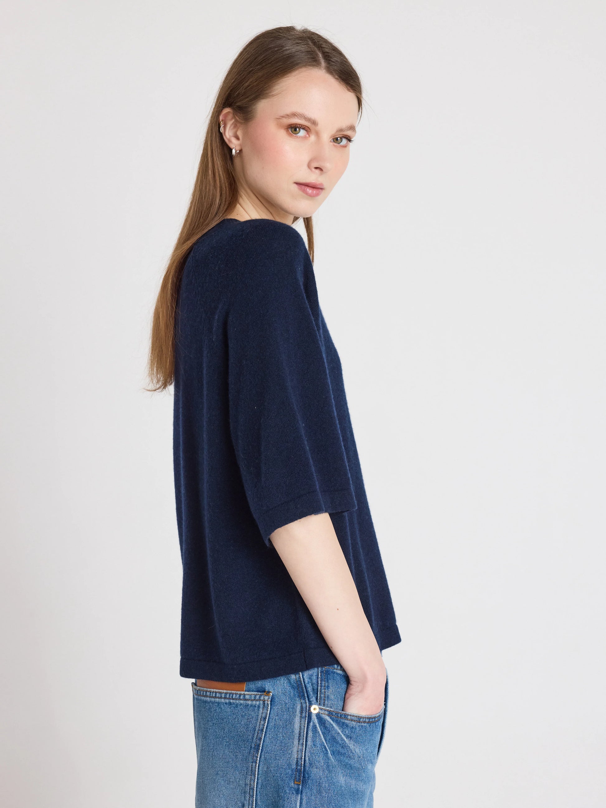 Woman wearing a navy blue sweater and jeans on a light gray background