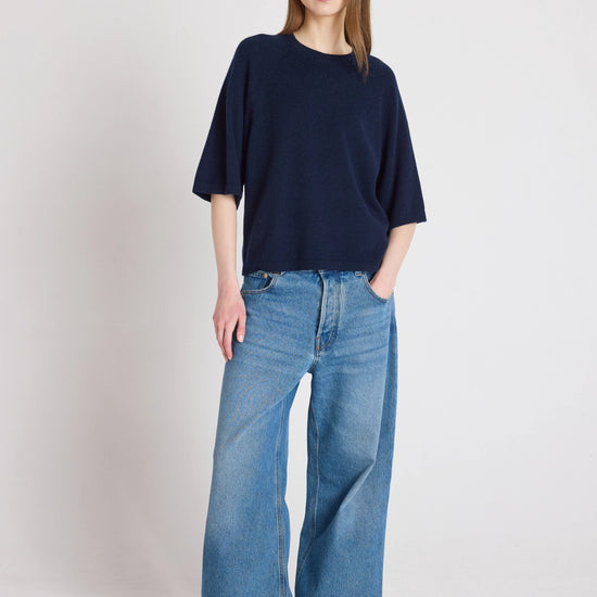 Person wearing a navy sweater and blue jeans on a white background