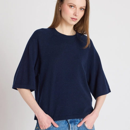 Woman wearing a navy blue oversized sweater and blue jeans on a plain background