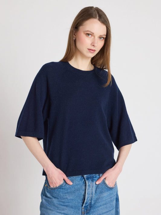Woman wearing a navy blue oversized sweater and blue jeans on a plain background