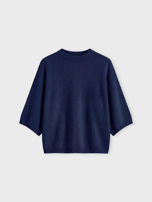 A navy blue knit sweater with wide, draped sleeves and a crew neck, displayed flat against a light gray background.
