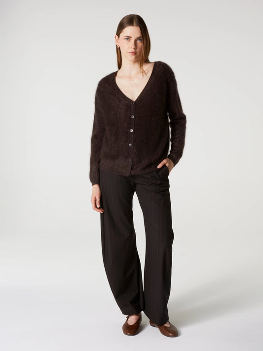 A woman modeling a dark brown fuzzy V-neck cardigan with buttons and matching dark brown wide-leg trousers, standing against a light gray studio background.