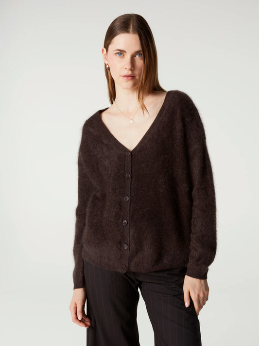 A woman modeling a dark brown fuzzy button-up cardigan sweater with a V-neck, paired with black pants, against a plain light gray studio background.