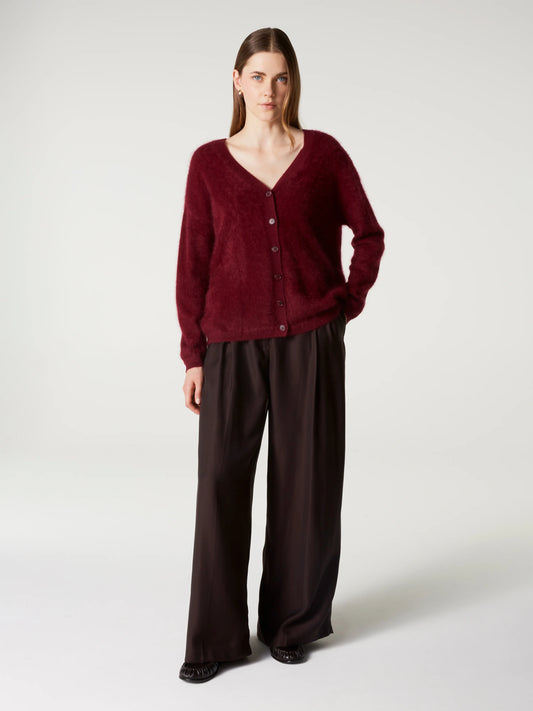 A woman stands against a light gray studio background wearing a fuzzy long-sleeve button-front cardigan in deep burgundy and wide-leg dark brown pants.