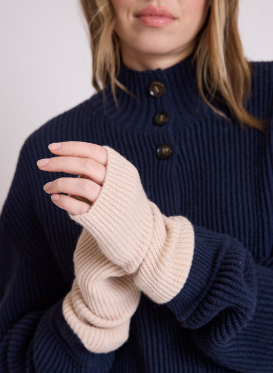 A close-up of a person wearing a navy ribbed knit mock-neck sweater with dark buttons and cream ribbed knit fingerless wrist cuffs.