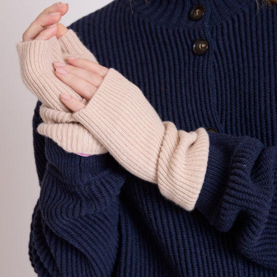 A close-up of a person wearing cream ribbed knit fingerless gloves over a navy blue ribbed knit sweater with dark buttons.