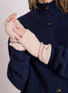 A close-up of a person wearing cream ribbed knit fingerless gloves over a navy blue ribbed knit sweater with dark buttons.