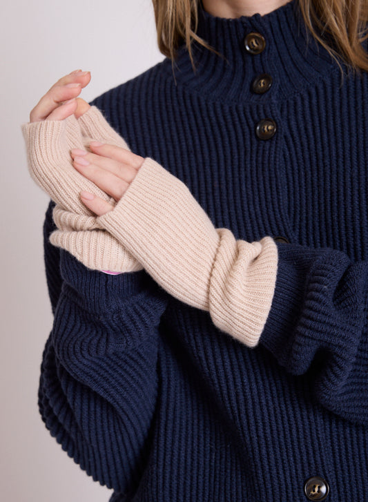 A close-up of a person wearing cream ribbed knit fingerless gloves over a navy blue ribbed knit sweater with dark buttons.