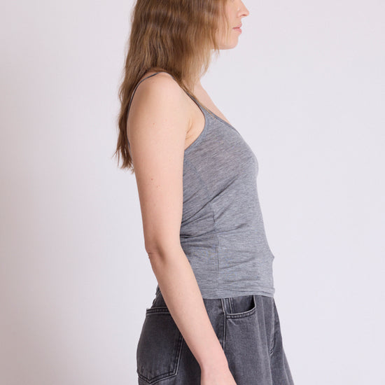 A woman shown in side profile wearing a heather gray ribbed tank top and dark gray denim skirt against a plain light gray studio background.