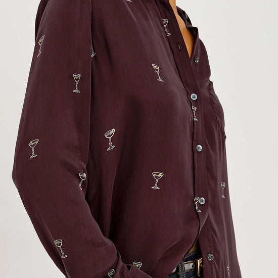 a model wearing A long-sleeve button-up shirt in deep burgundy with a repeating small white cocktail glass pattern,