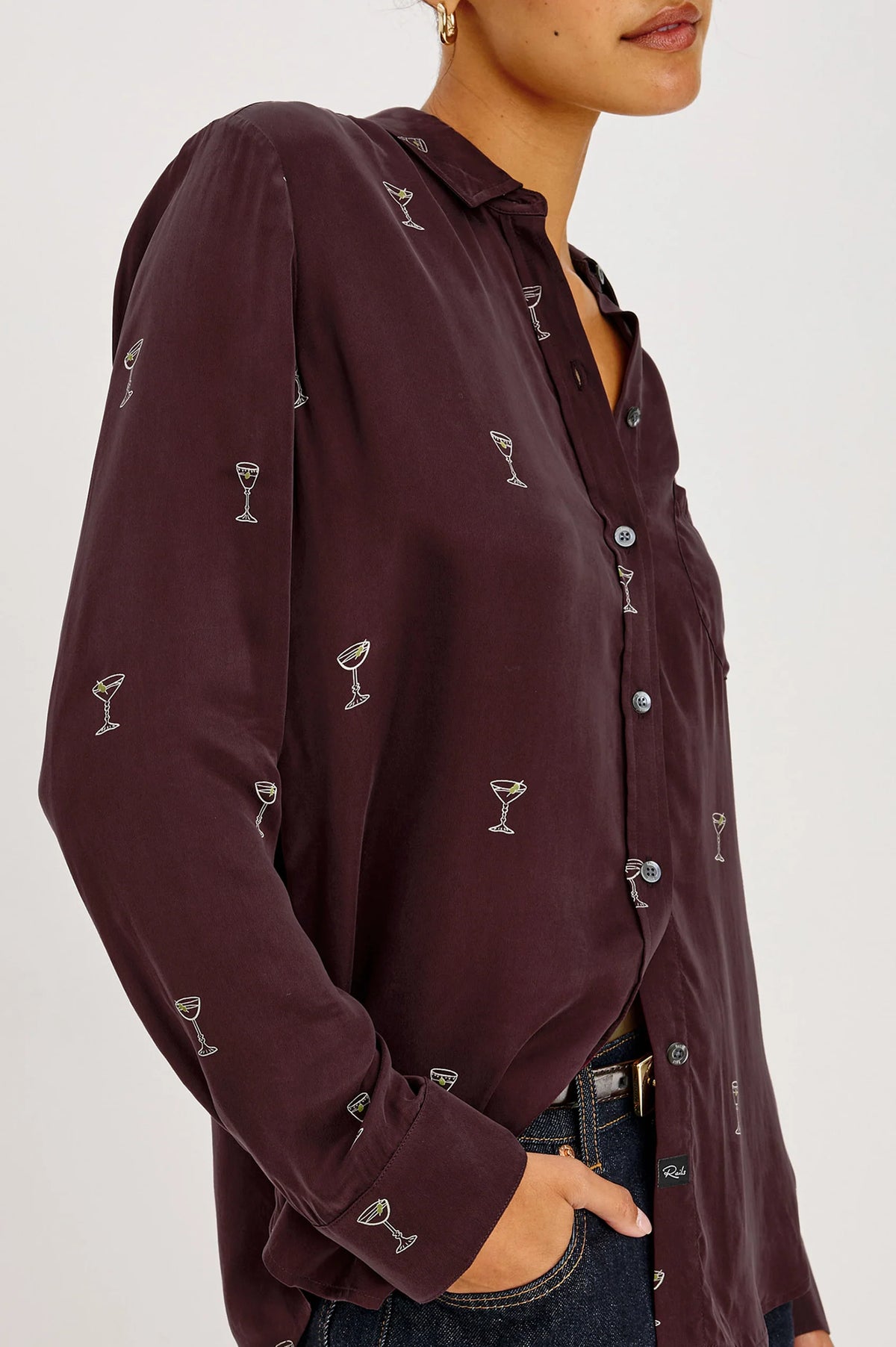 a model wearing A long-sleeve button-up shirt in deep burgundy with a repeating small white cocktail glass pattern,