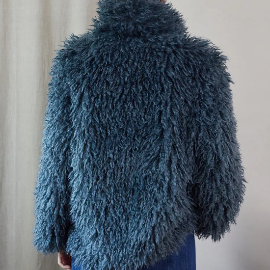 Blue faux fur short jacket worn with blue jeans rear view