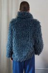 Blue faux fur short jacket worn with blue jeans rear view