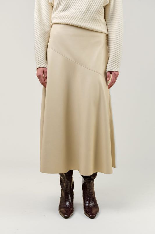 A model is shown from the chest down wearing a beige wrap-style midi skirt, a cream ribbed sweater, and dark brown boots, set against a plain light gray studio background.