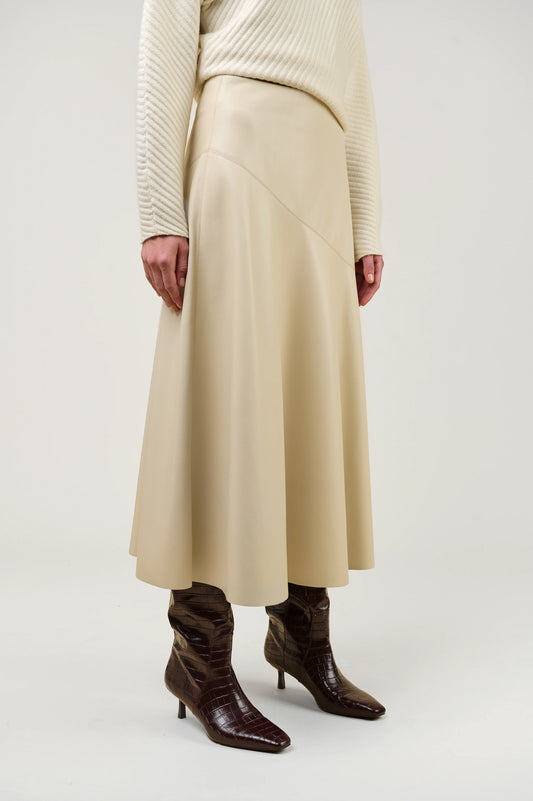 A model wearing a cream-colored pleated midi skirt, a cream ribbed sweater, and dark brown pointed-toe heeled boots, shown from the waist down against a light gray studio background.