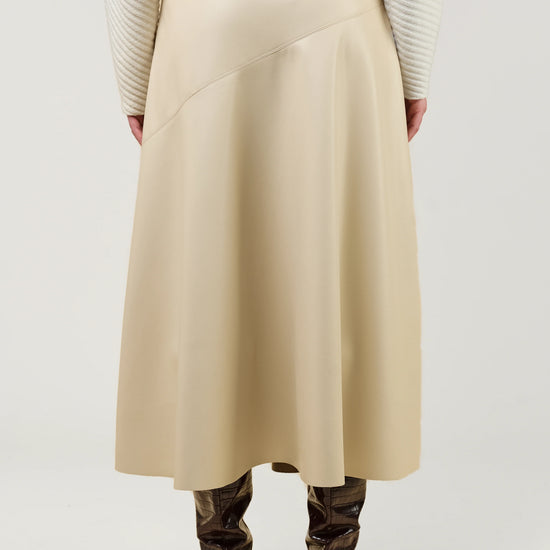 A person shown from the back wearing a long cream ribbed sweater, a beige wrap-style midi skirt, and brown heeled ankle boots against a light gray studio background.