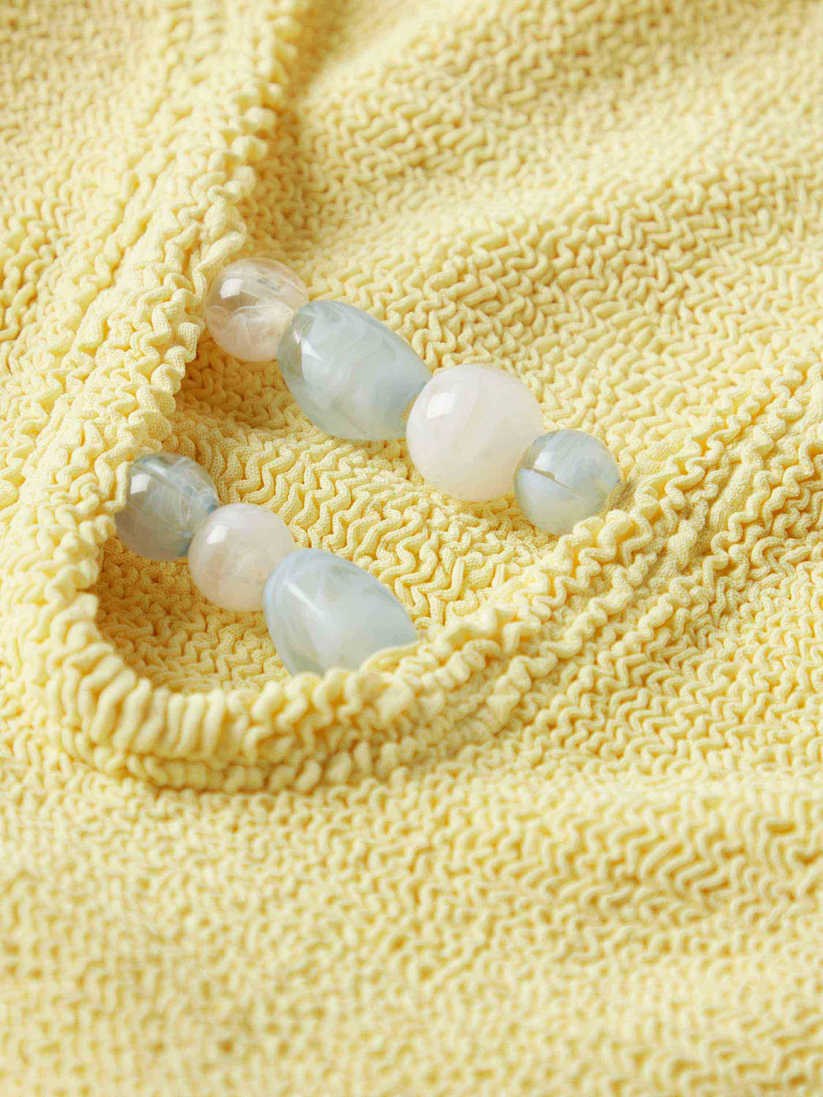 Close up detail of blue bead detail on one size yellow swimsuit from Hunza G