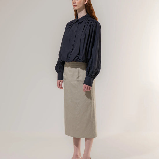 Woman wearing a navy blouse and beige skirt against a plain background