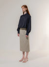 Woman wearing a navy blouse and beige skirt against a plain background