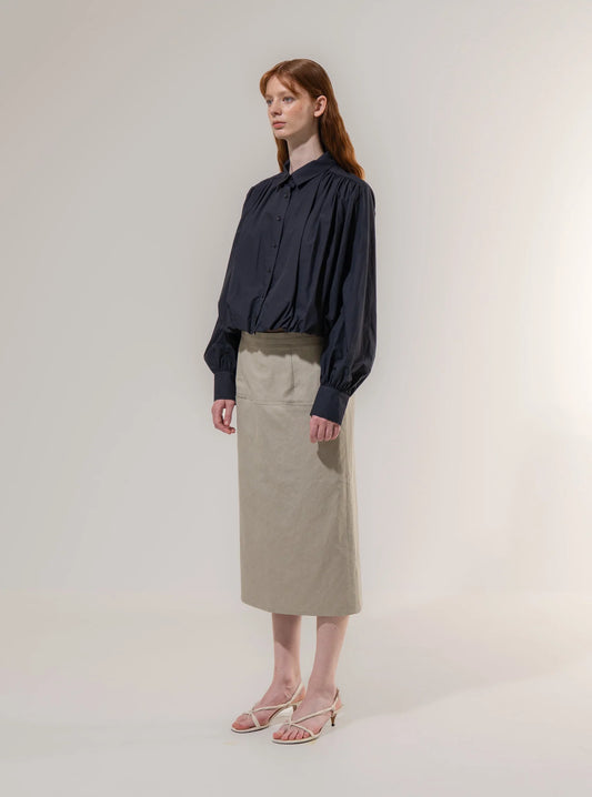 Woman wearing a navy blouse and beige skirt against a plain background