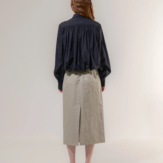 Person wearing a navy shirt and beige skirt on a white background