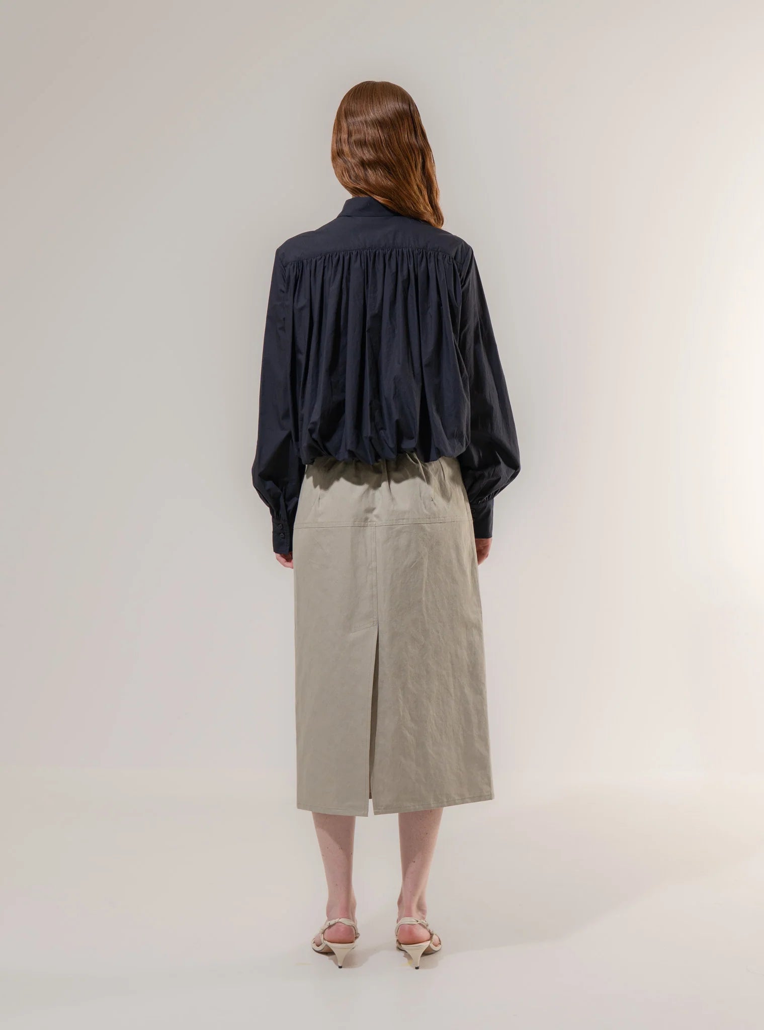 Person wearing a navy shirt and beige skirt on a white background