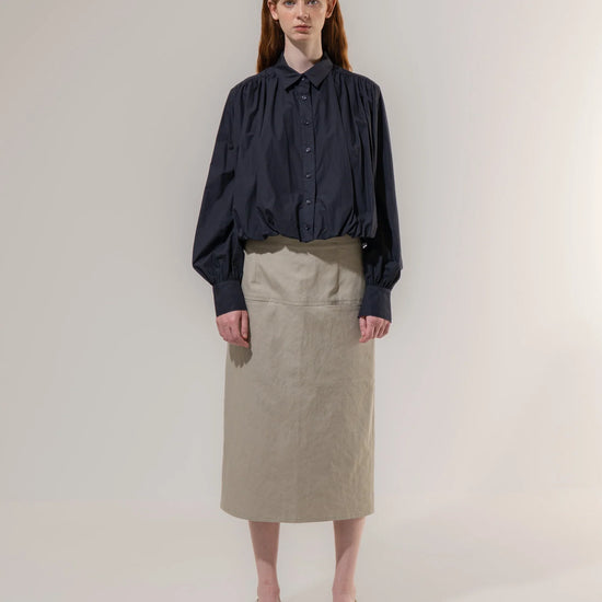Woman wearing a dark blouse and beige skirt on a plain background
