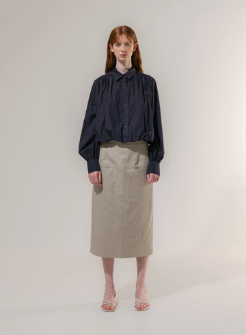 Woman wearing a dark blouse and beige skirt on a plain background