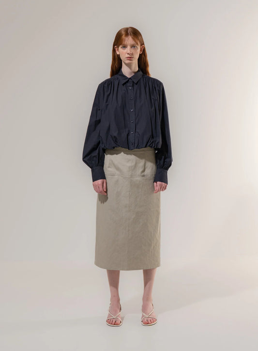 Woman wearing a dark blouse and beige skirt on a plain background