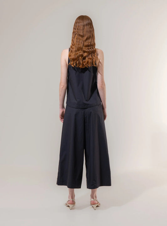 Person wearing a black sleeveless top and wide-leg pants on a plain background