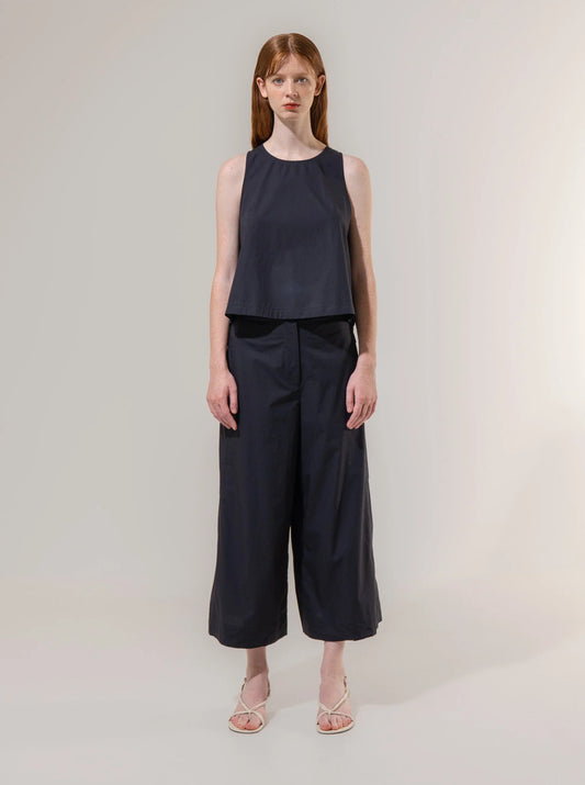 Woman wearing a navy sleeveless top and wide-leg pants on a plain background