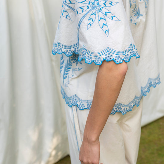 White outfit with blue embroidery against a white curtain background