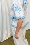 White outfit with blue embroidery against a white curtain background