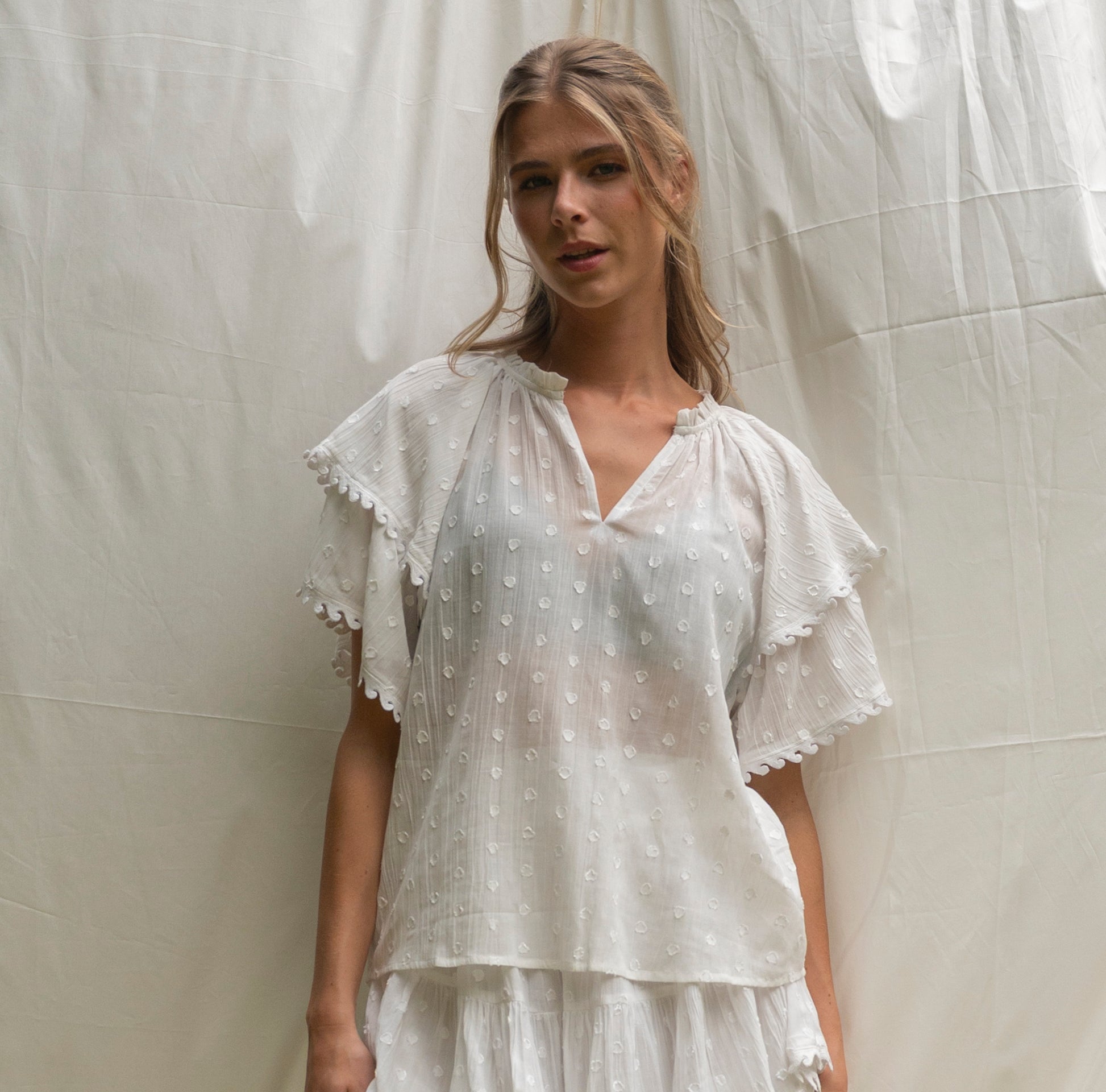 Woman wearing a white blouse with ruffled sleeves against a neutral background