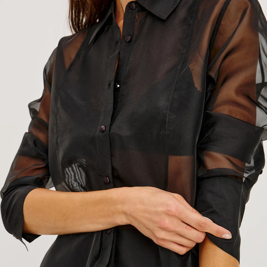 close up of a Model wearing a sheer black button up shirt with a black slip skirt 