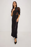 full body shot of a Model wearing a sheer black button up shirt with a black slip skirt and black pointed toe shoes 