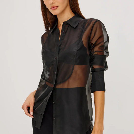 Model wearing a sheer black button up shirt with a black slip skirt 