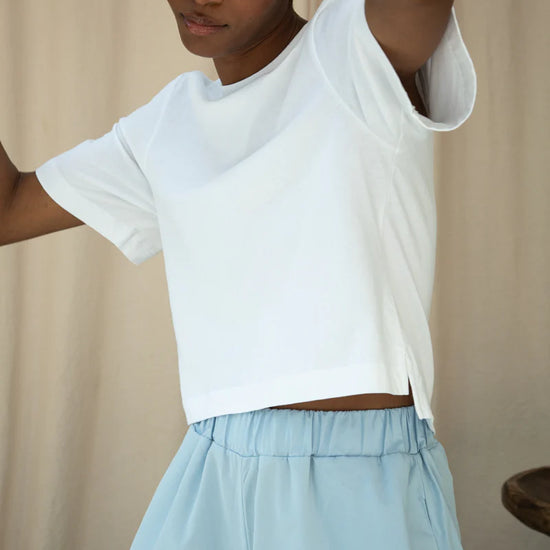 Person wearing a white crop top and light blue skirt against a beige background