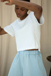 Person wearing a white crop top and light blue skirt against a beige background