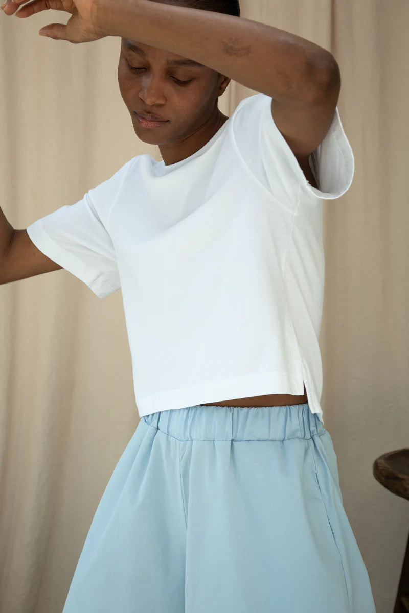 Person wearing a white crop top and light blue skirt against a beige background